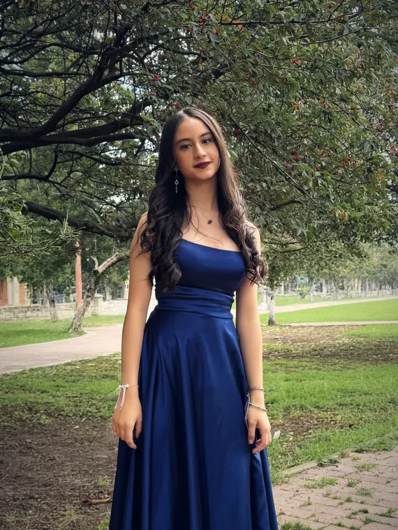 Paula sonríe bajo un árbol, con su vestido azul de satín y aretes largos
